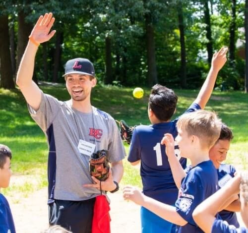 True-Ground-Group-Volunteers-Volunteering-FAQs Coach leading kids in a baseball practice outdoors