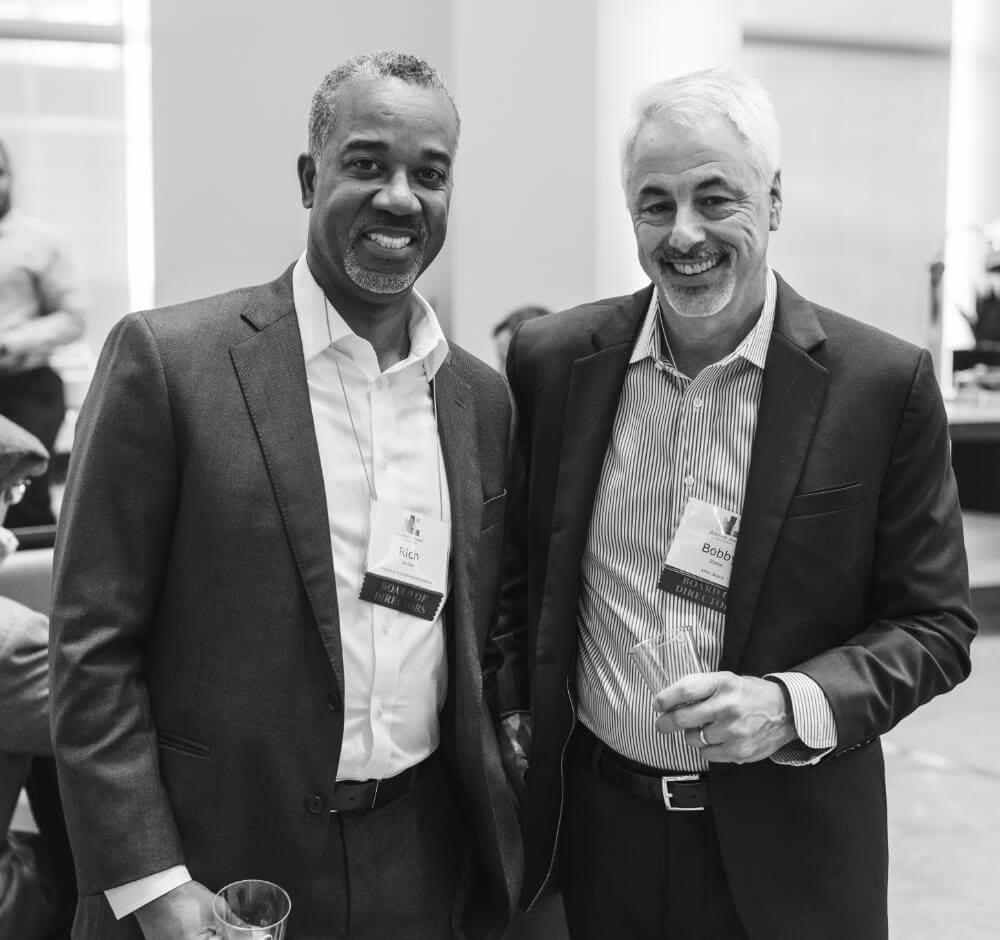 Two men in business attire smiling at a networking event