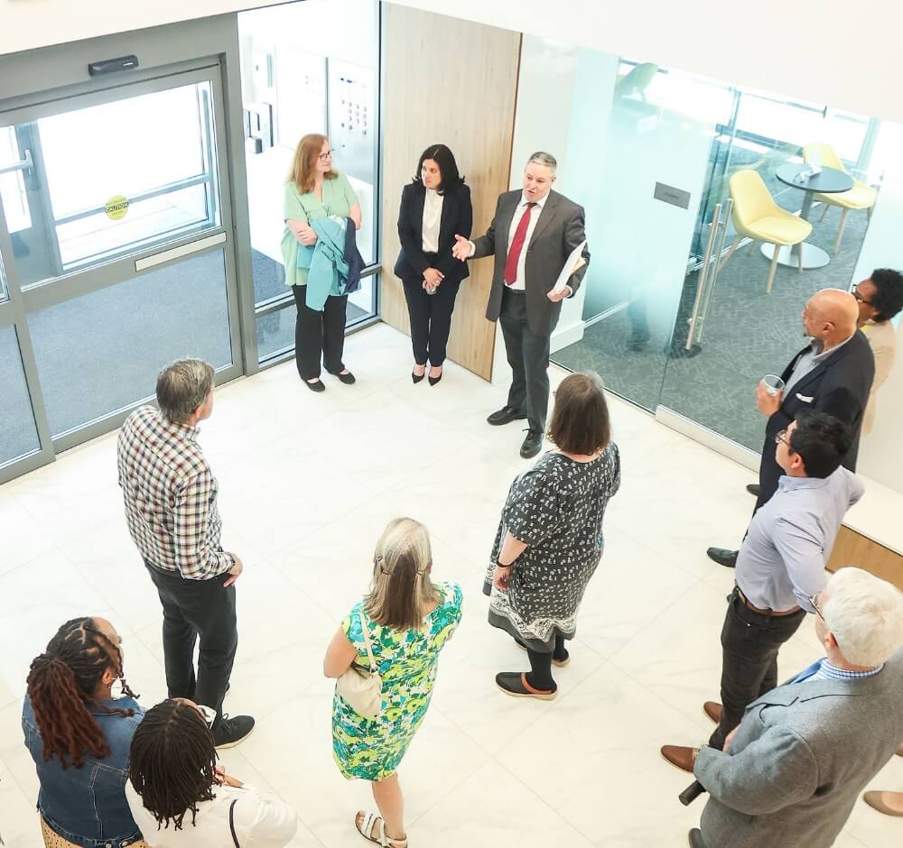 True-Ground-Tribute-Gifts-Donor-FAQs@2x Group of people having a discussion in a building lobby