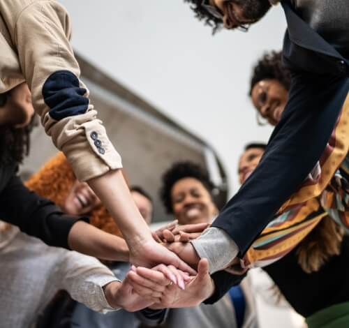 True-Ground-Volunteer – Groups-Together Diverse group of people in a circle, hands joined in unity