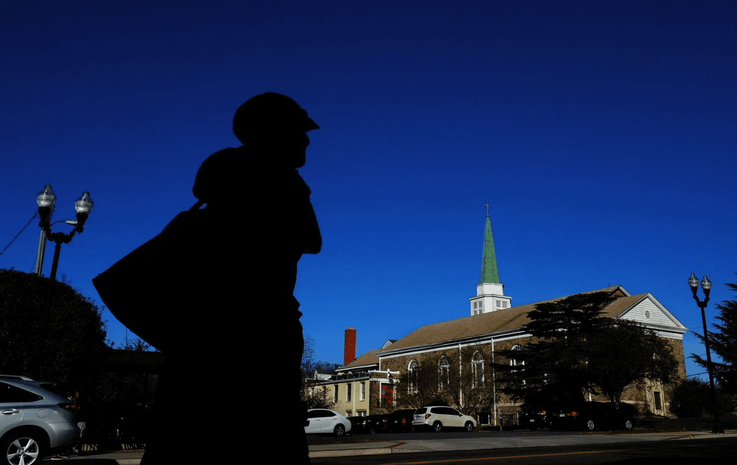 Silhouette of a person with a church steeple in the background against a clear blue sky