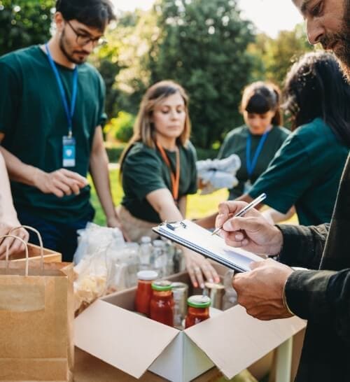 How-To-Help–Host-a-Donation-Drive-Group-Donations@1x Group of volunteers in green shirts organizing and inventorying donation items.