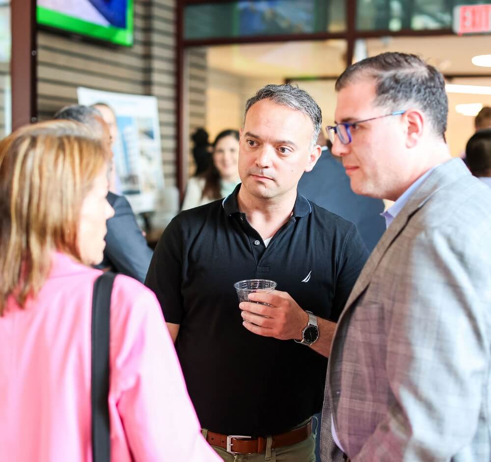 Three people having a conversation at a networking event, with a man holding a drink and others listening