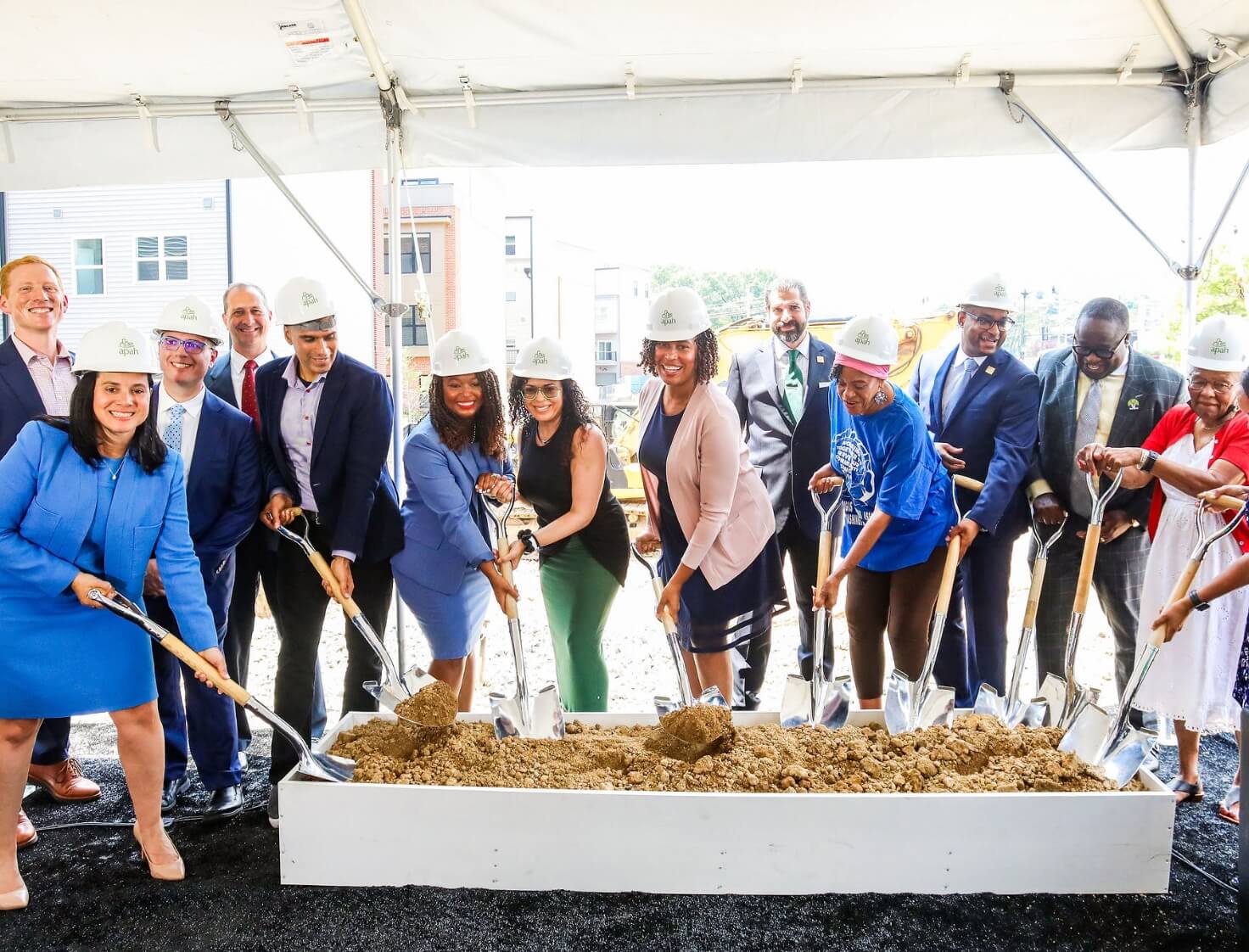 Group of officials breaking ground on construction project, wearing helmets and holding shovels.