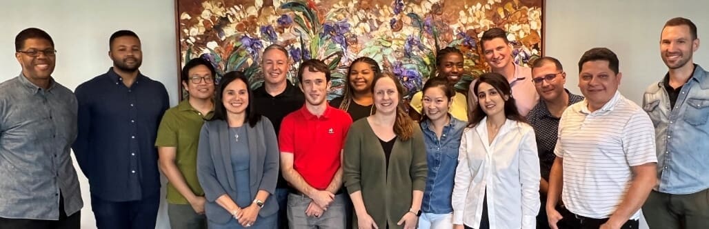 Group photo of smiling team members in front of a colorful artwork