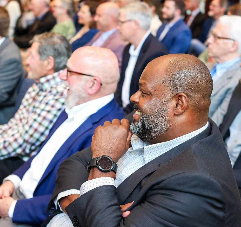 True-Ground-IRA-Donor-FAQs@2x Audience members smiling and engaged during a presentation