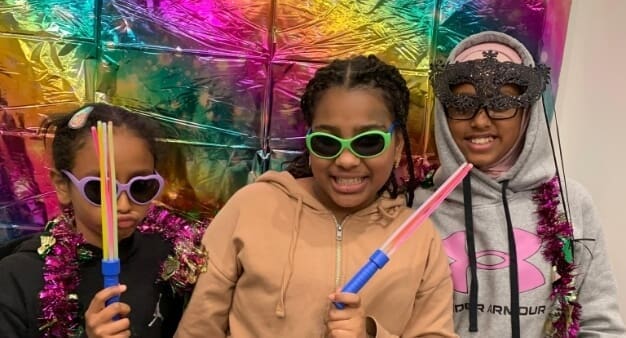 three girls in fun accessories posing in front of a colorful backdrop at a party