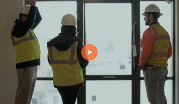 True-Ground-Partner-with-Real-Estate-Terwilliger-Place-Video@2x Screenshot of a video showing workers dressed in safety suits.