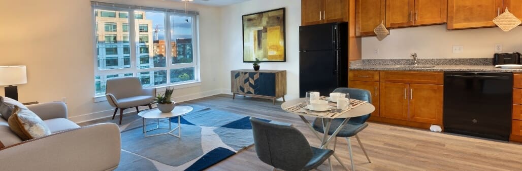 Brightly lit modern living room and kitchen area with large windows.