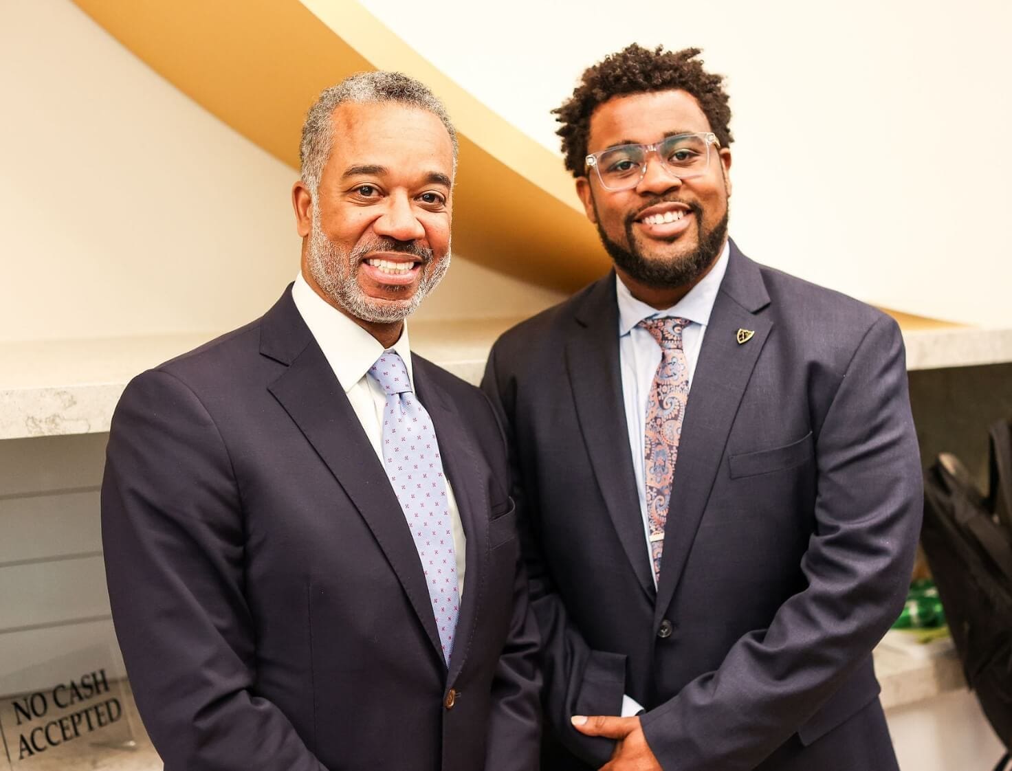 Two men in suits smiling at the camera during a professional event.