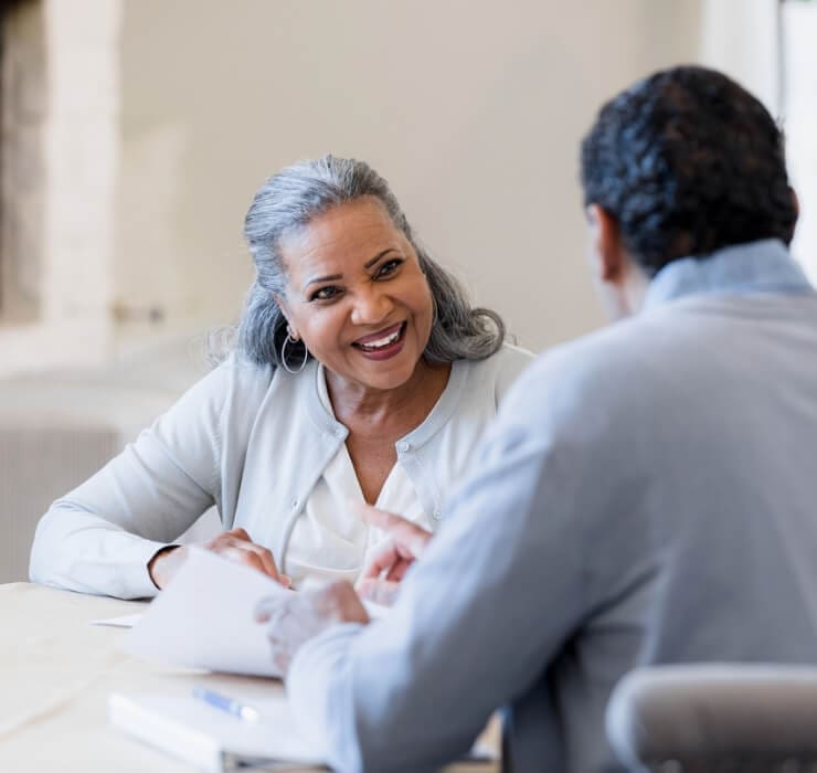 Smiling elderly woman engaging in conversation with another person at a table