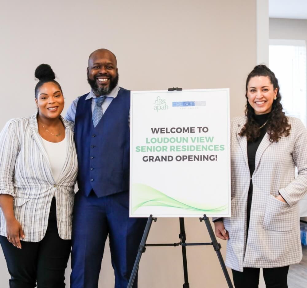 Three people smiling beside a sign that reads "Welcome to Loudoun View Senior Residences Grand Opening!