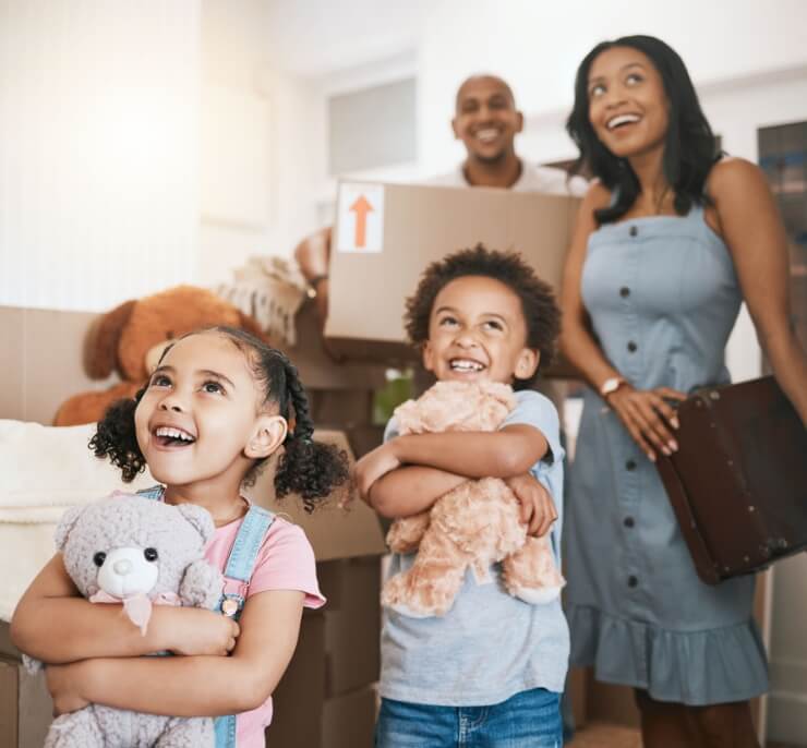 Happy family with two children moving into a new home, surrounded by boxes and holding teddy bears