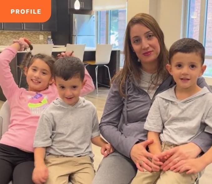 A woman sits with three kids in a kitchen. An orange "profile" label appears in the top left corner.